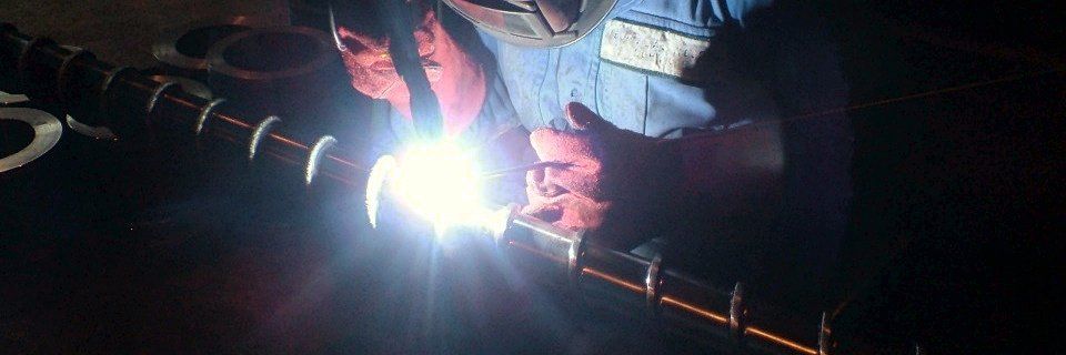 Welder hardfacing a feedscrew flight under a bright welding arc